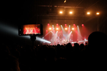 Backlit stage with vibrant lights at outdoor music festival. Fans record live performance on smartphones. Excitement in air, band plays hit songs. Summer night event