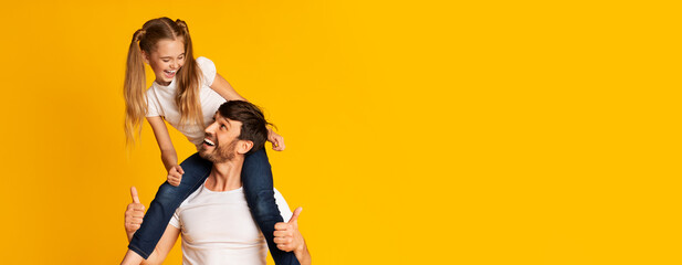Obraz premium A father carries his smiling daughter on his shoulders, both enjoying a cheerful moment together. The vibrant yellow backdrop enhances their lively expressions, highlighting their bond and joy.