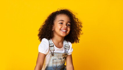 Laughing cute afro girl portrait, kid hearing joke over yellow studio background