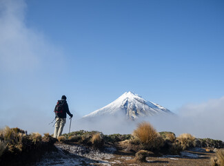Obraz premium Man looking at Snow-capped Mt Taranaki in the clouds. Pouakai Circuit track. New Zealand.