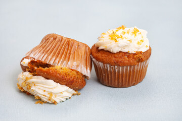Two carrot cupcakes, one upside down squashed one. Light pastel blue background