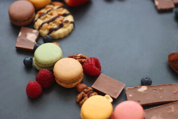 Macarons, chocolate, cookies, berries and various nuts on dark blue background. Selective focus.