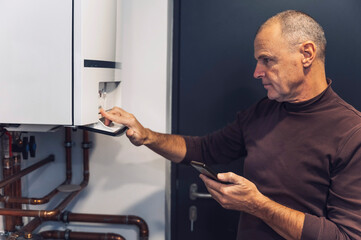 A man adjusting a digital timer on a wall-mounted heating control panel. The panel features...
