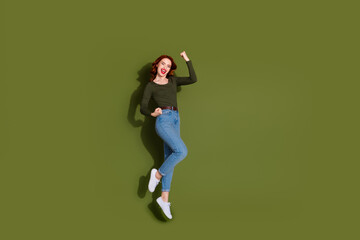 Full length photo of charming lucky lady wear shirt jumping high rising fists empty space isolated...