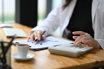 Cropped shot female accountant making calculations and preparing financial data report at desk