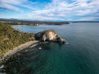 Aerial view of coastal landscape with rocky cliff and clear blue waters.