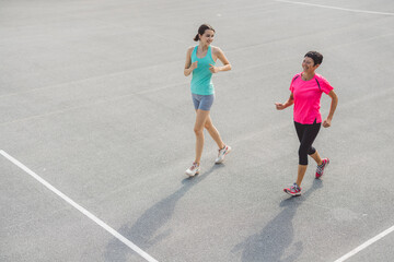 Fototapeta premium Two women jogging together on a sports court, one in a light blue tank top and shorts, the other in a pink shirt and black leggings. They appear to be enjoying their exercise routine.