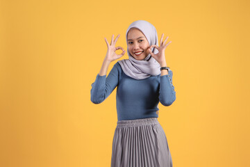 happy asian indonesian muslim woman giving ok finger gesture on isolated yellow background