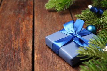 Fir tree branches with Christmas decor and gift box on wooden table, closeup. Space for text