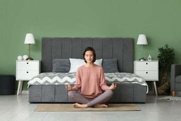 Young woman meditating while sitting on floor in bedroom