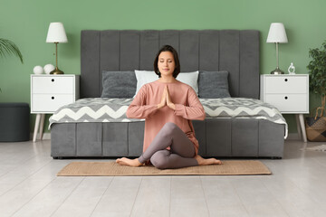 Young woman meditating while sitting on floor in bedroom