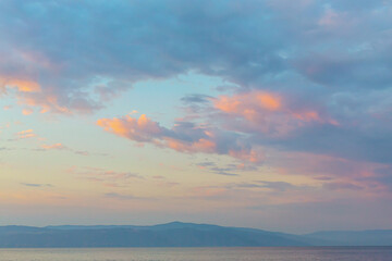 Serene sunrise over calm sea with pastel clouds and distant mountains, perfect for background or wallpaper