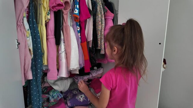 little girl choosing clothes from the wardrobe. Girl choosing dress a lot of clothes in the child wardrob