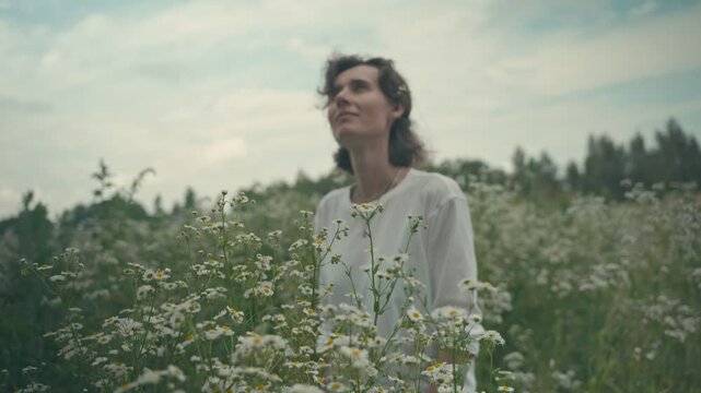 A girl in a white T-shirt standing in a field of daisies looking at the sky, sneezing, laughing, medium shot