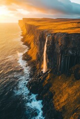 Aerial view of a dramatic cliffside waterfall cascading into the ocean at sunset.