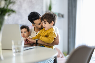 Father and his little kids using laptop at home together
