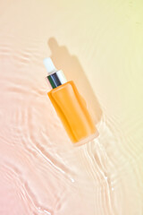 A glass bottle filled with a liquid sits on a water ripple and gradient surface of pink and orange. This image creates a dreamy atmosphere, ideal for promoting skincare products.