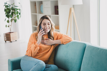 Fototapeta premium Photo portrait of nice cheerful girl sit couch talk phone laugh dressed orange garment spend pastime spacious house indoors room