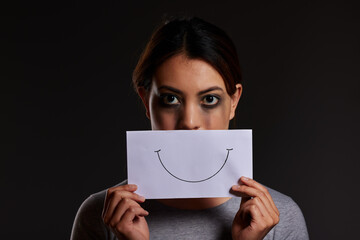 Sad woman, portrait and abuse with fake smile for trauma or domestic violence in studio on a black...