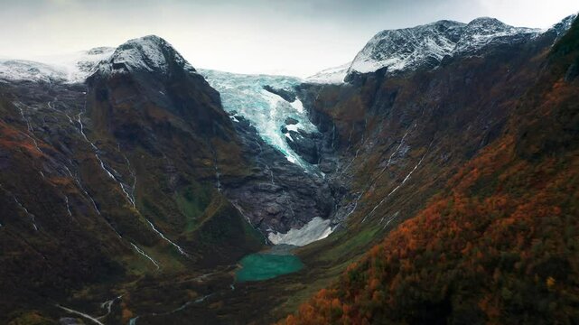 A dynamic landscape featuring a glacier, rocky cliffs, and the warm tones of autumn leaves, with water cascading down the mountainsides.