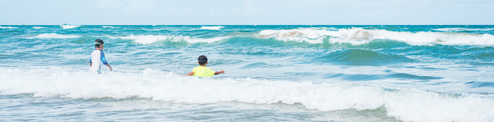 Panorama rear view Asian toddler boy playing with wave, turquoise water at tropical beach South Padre Island, Texas, active outdoor activity, Vietnamese kid in swimming wear and goggles ocean