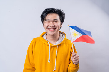 An Asian man in a yellow hoodie stands against a white background, smiling widely while holding the Philippine flag. He displays a sense of pride and joy, representing his nationality