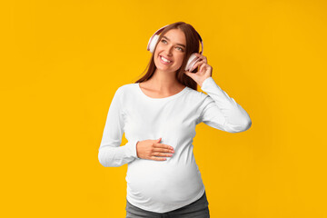 Music In Pregnancy. Smiling Expectant Girl In Headphones Listening To Song Over Pink Background. Studio Shot