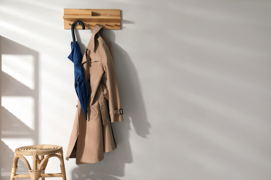 Colorful umbrella and trench coat hanging on rack at home. Space for text - Powered by Adobe