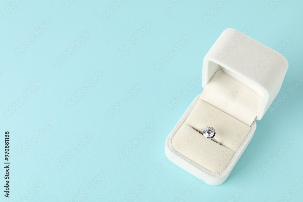 Poster Beautiful ring with gemstone in box on light blue background, above view. Space for text