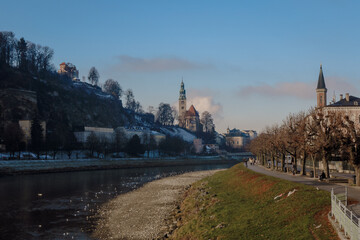 Obraz premium Winter landscape of Salzburg along the riverbanks with historic architecture and serene winter scenery at dusk
