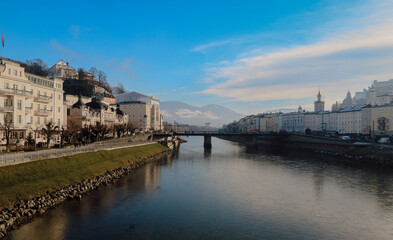 Obraz premium A serene winter morning in Salzburg with snow-covered buildings and a peaceful river promenade