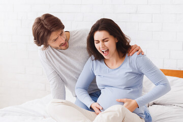 Prenatal contractions. Worried husband comforting pregnant wife that suffering from acute pain on bed at home, she is giving birth, copy space