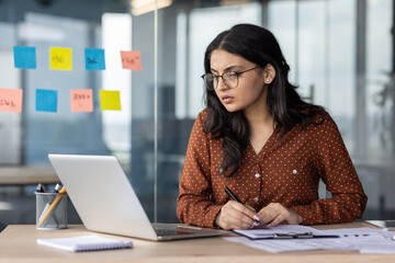 Serious thinking and concentrated focused business woman behind paper work inside office. An...