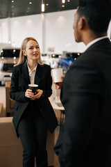 Vertical shot of successful multiethnic business people in formal outfit having break after meeting, talking during drinking coffee together in auto dealership. Concept lifestyle of businesspeople.