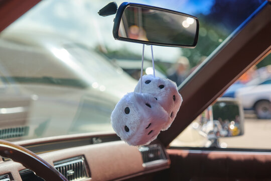 Two white furry dice under the rear view mirror of a classic American retro oldtimer car as a luck symbol.