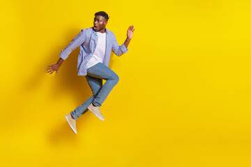 Fototapeta premium Full length photo of funky cool guy dressed checkered shirt jumping high emtpy space isolated yellow color background
