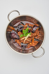 Spicy eggplant curry cooked with aromatic spices and garnished with fresh ginger and mint in a stainless steel pot