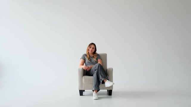 Portrait of a laughing young Caucasian woman relaxing on armchair and having fun on white background. Happy people with positive emotions.