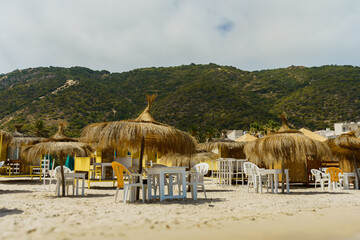 Grass umbrella and wooden tables on white sand beach