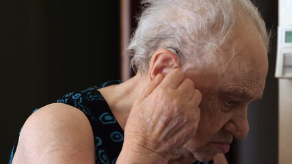 A 90-year-old woman inserting a hearing aid into her ear. Focus on the careful process of improving her hearing - Powered by Adobe