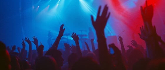 A lively crowd enjoys a music concert under dynamic blue and red stage lights, capturing the essence of energy and musical euphoria.