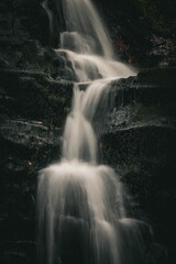 Obraz premium Serene waterfall cascading over moss-covered rocks in a dark forest setting