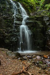 Fototapeta premium Serene waterfall cascading over moss-covered rocks in a lush forest setting