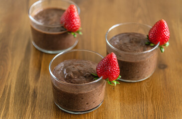 chocolate pudding in glasses decorated with ripe fragrant strawberries on a wooden table shallow...