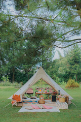 Rustic and romantic luxury picnic with teepee in the middle of a pine forest. White tent with decorated light and hay seat for recreation outdoor with lake and green forest background. © Andri