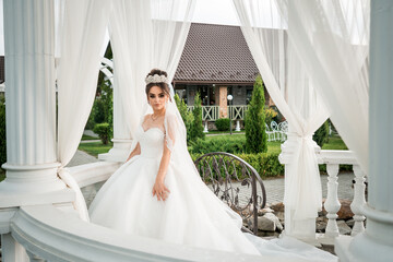 Elegant Bride in Classic White Gown Standing Gracefully Under Draped Pavilion Curtains at Scenic...