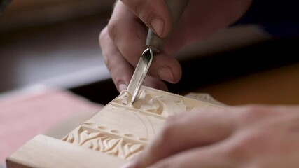Wood carving. Hand of a man wood carving master holds a cutting tool to applying floral patterns and ornaments on a wooden box. Concept of handicraft as a hobby, skill, talent and exquisite artwork.