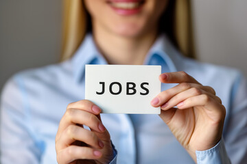 Woman is holding a card that says "jobs" in white letters. She is smiling and she is happy