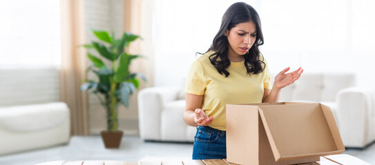 A middle eastern woman with a puzzled expression examines a cardboard box in her living room,...
