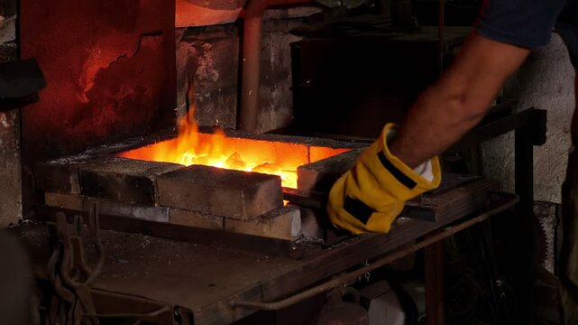 A red-hot metal product on a fire made of anthracite coals. The blacksmith puts metal rods on the fire in the forge.